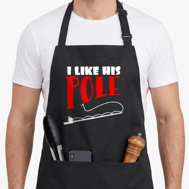 Pole couple apron - I LIKE HIS POLE text in red and white above fishing rod line art — shown on a black cotton canvas apron against a white background