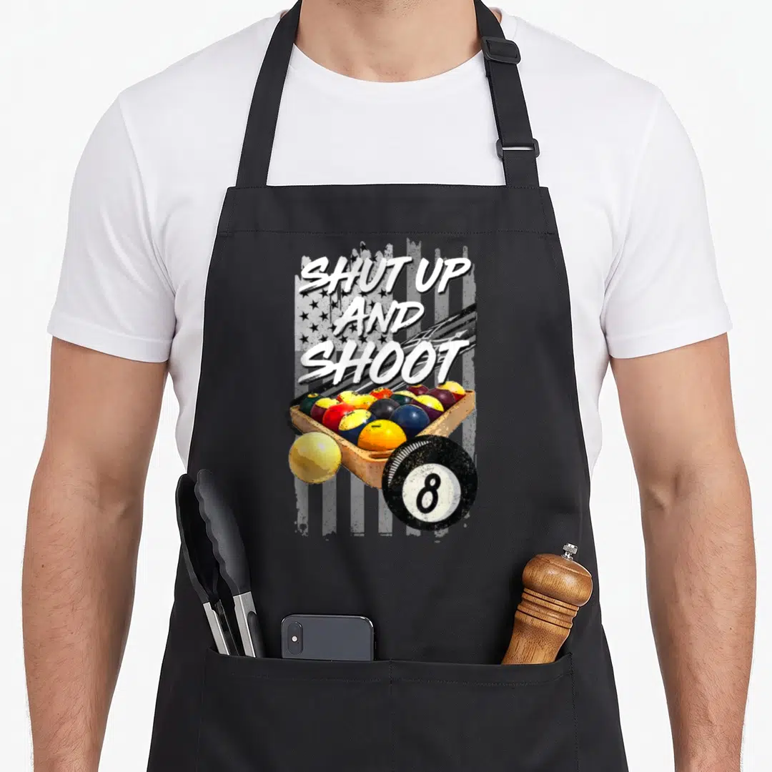 Shut billiards apron - SHUT UP AND SHOOT text over grayscale flag and wooden billiard ball tray with 8-ball — shown on a black cotton canvas apron against a white background