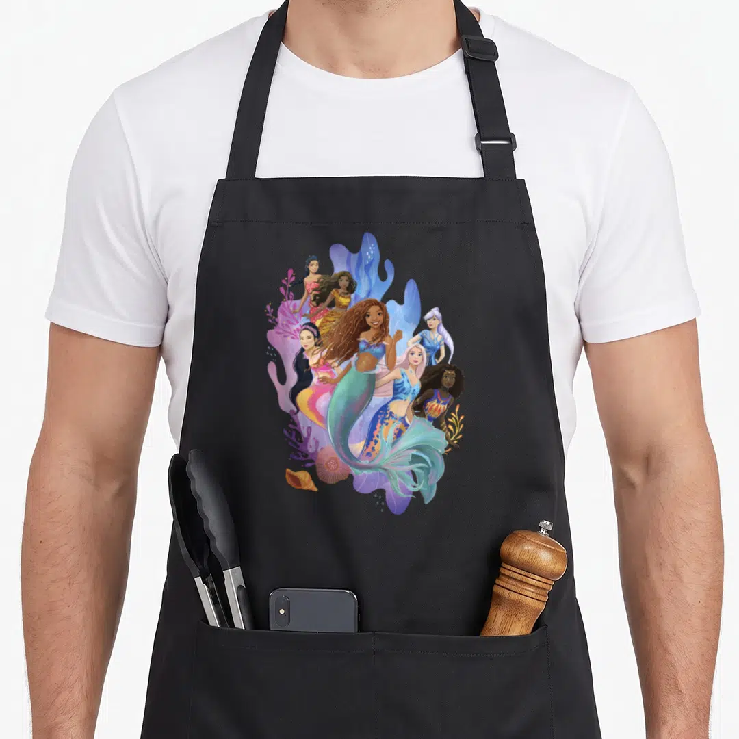 Sister mermaid apron - Six cartoon mermaids in blue, purple, pink, and teal surrounded by purple coral and a seashell — shown on a black cotton canvas apron against a white background