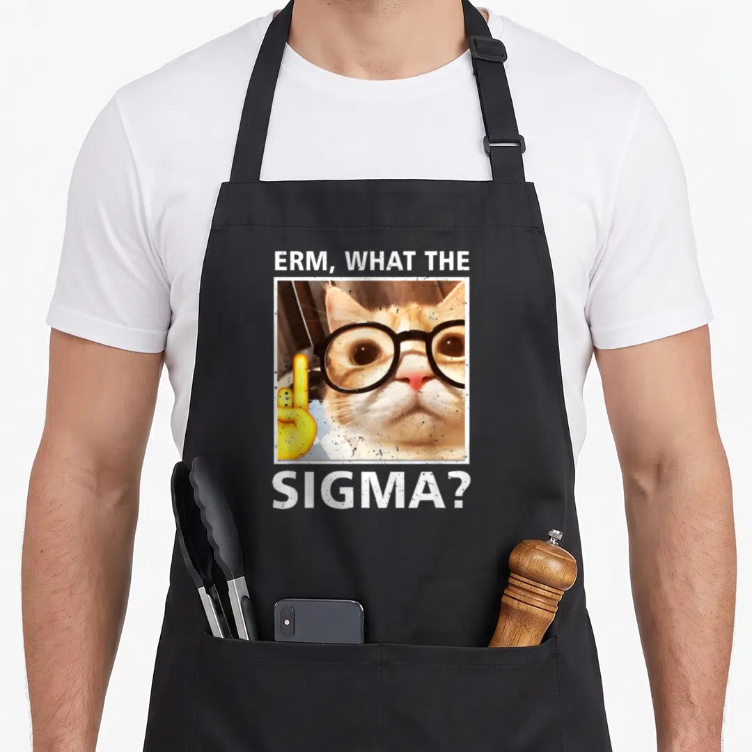 Erm funny cat apron - Cat in black glasses with ERM WHAT THE SIGMA text and yellow hand emoji in white frame — shown on a black cotton canvas apron against a white background