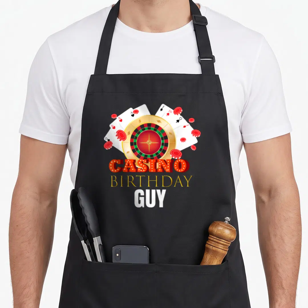 Casino chef outfit with apron - Roulette wheel, fanned cards, chips, and stacked Casino Birthday Guy text in red gold — shown on a black cotton canvas apron against a white background
