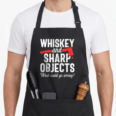 Lumberjack throwing apron - Whiskey and sharp objects text with red axe graphic and blood drop on black fabric — shown on a black cotton canvas apron against a white background