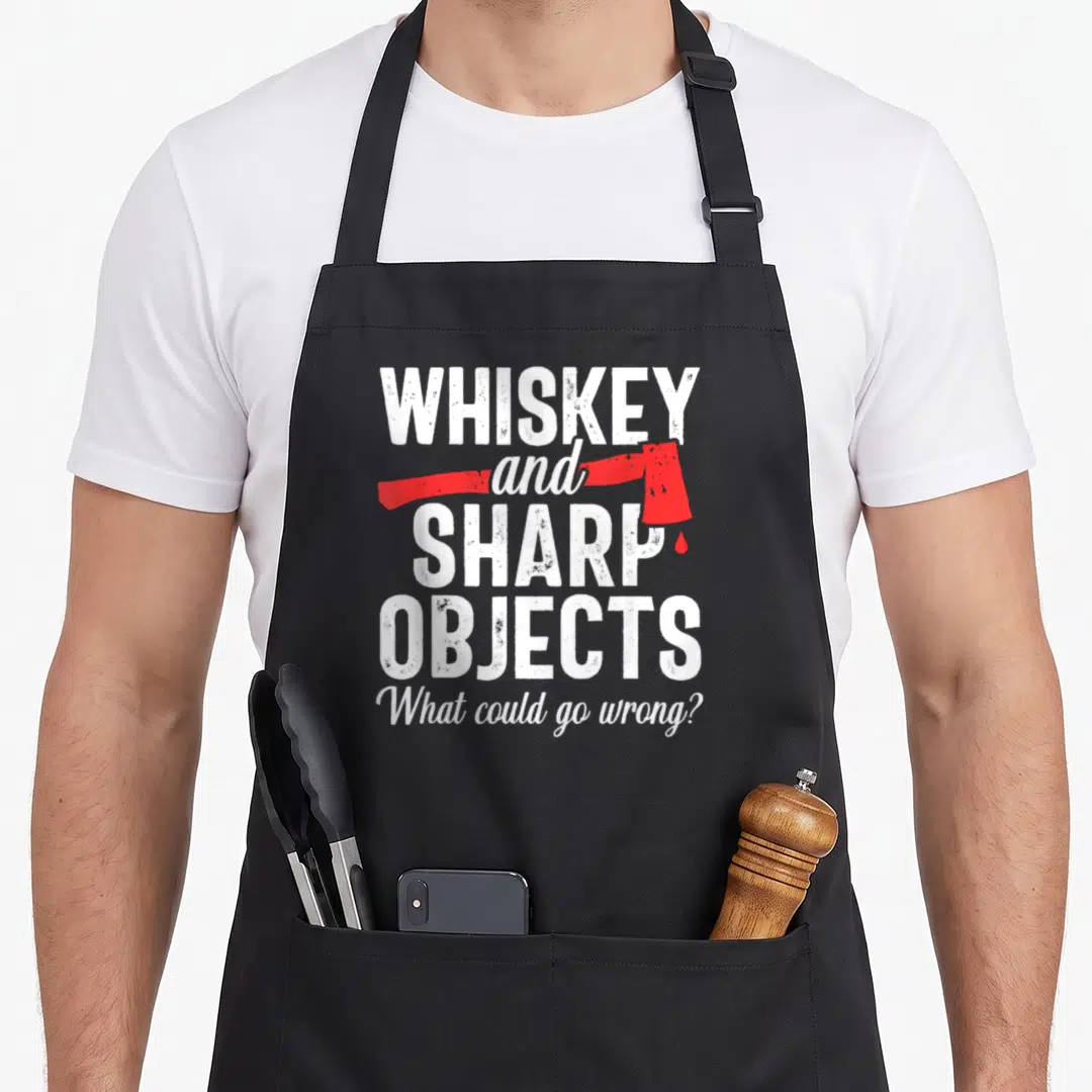 Lumberjack throwing apron - Whiskey and sharp objects text with red axe graphic and blood drop on black fabric — shown on a black cotton canvas apron against a white background