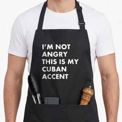 Cuban cuba apron - White stacked text I'M NOT ANGRY THIS IS MY CUBAN ACCENT on dark background — shown on a black cotton canvas apron against a white background
