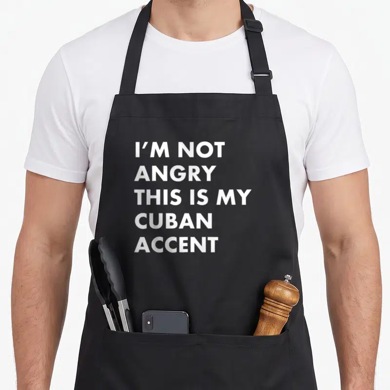 Cuban cuba apron - White stacked text I'M NOT ANGRY THIS IS MY CUBAN ACCENT on dark background — shown on a black cotton canvas apron against a white background