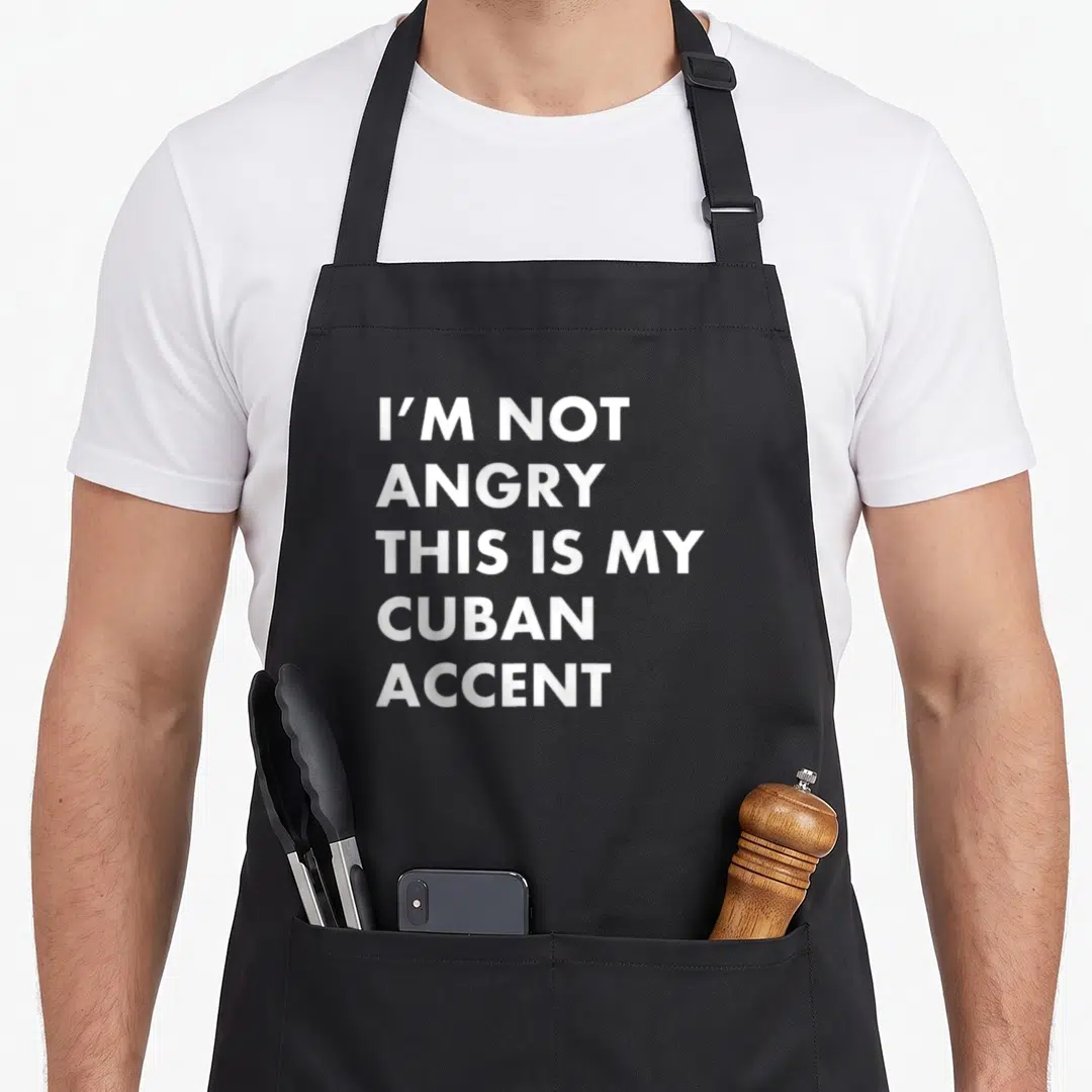 Cuban cuba apron - White stacked text I'M NOT ANGRY THIS IS MY CUBAN ACCENT on dark background — shown on a black cotton canvas apron against a white background