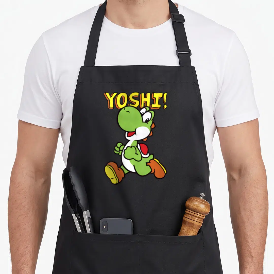 Funny intro jump apron - Green cartoon dinosaur running below yellow arched YOSHI! text — shown on a black cotton canvas apron against a white background