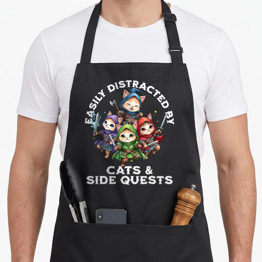 Quest cat apron - Four cartoon cats in blue green red purple robes holding weapons under white text — shown on a black cotton canvas apron against a white background