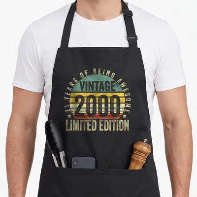 Edition 21st birthday apron - Retro text design reading 21 years of being awesome vintage 2000 limited edition — shown on a black cotton canvas apron against a white background
