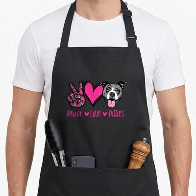 Matter dog apron - Peace Love Pitties text below peace sign heart and dog head in pink grey white — shown on a black cotton canvas apron against a white background