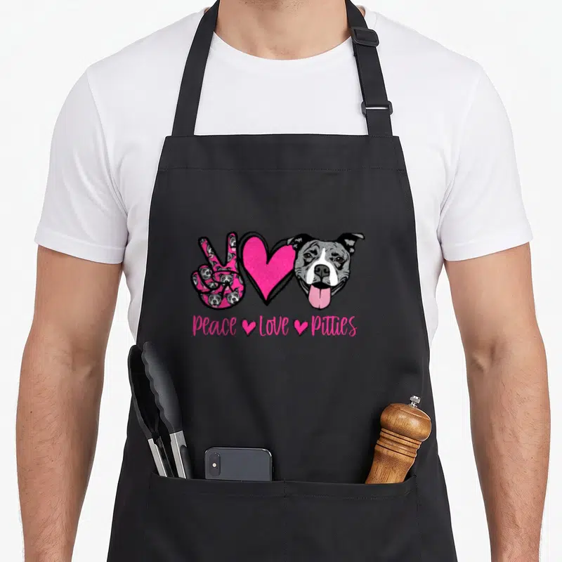 Matter dog apron - Peace Love Pitties text below peace sign heart and dog head in pink grey white — shown on a black cotton canvas apron against a white background