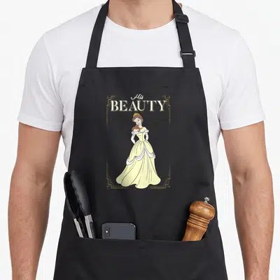 Belle couple apron - Cartoon woman in yellow dress with His BEAUTY text and gold frame — shown on a black cotton canvas apron against a white background