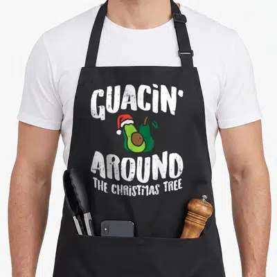 Boredkoalas christmas tree apron - Avocado in Santa hat with text GUACIN AROUND THE CHRISTMAS TREE — shown on a black cotton canvas apron against a white background