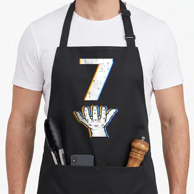 Number meme halloween apron - White number 7 above open hand with blue yellow orange glitch outlines — shown on a black cotton canvas apron against a white background