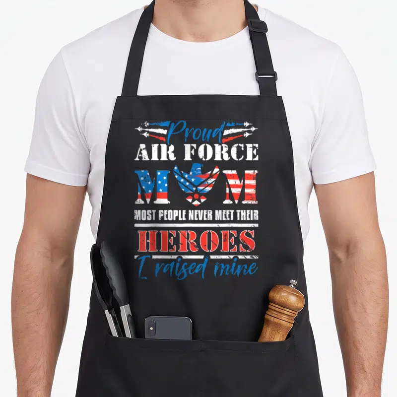Proud airman apron - Eagle and flag-patterned MOM text with Proud Air Force Mom heroes slogan in red white blue — shown on a black cotton canvas apron against a white background