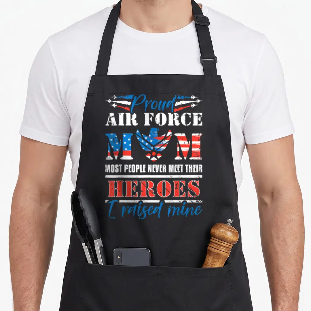 Proud airman apron - Eagle and flag-patterned MOM text with Proud Air Force Mom heroes slogan in red white blue — shown on a black cotton canvas apron against a white background