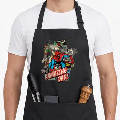 Funny amazing father day apron - Spider-Man crouching over comic pages with red AMAZING DAD! text below — shown on a black cotton canvas apron against a white background