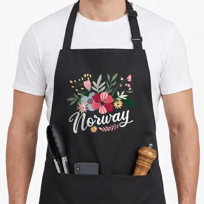 Country scandinavian aprons - Floral bouquet in white red blue green and yellow above Norway text — shown on a black cotton canvas apron against a white background