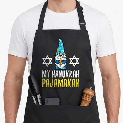 Chanukah hanukkah apron - Cartoon gnome holding dreidel between two stars with MY HANUKKAH PAJAMAKAH text — shown on a black cotton canvas apron against a white background