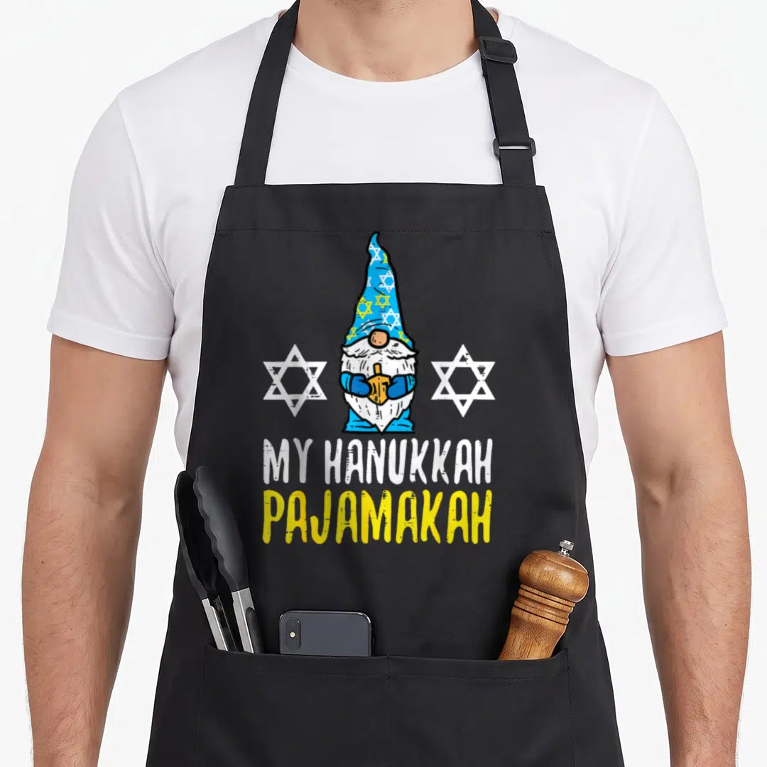 Chanukah hanukkah apron - Cartoon gnome holding dreidel between two stars with MY HANUKKAH PAJAMAKAH text — shown on a black cotton canvas apron against a white background