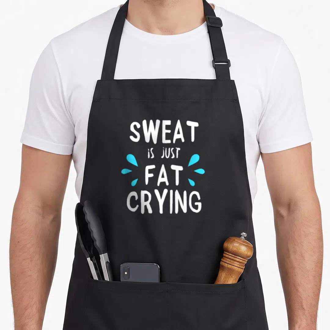 Sweat sweaty apron - White text SWEAT IS JUST FAT CRYING with light blue drops — shown on a black cotton canvas apron against a white background