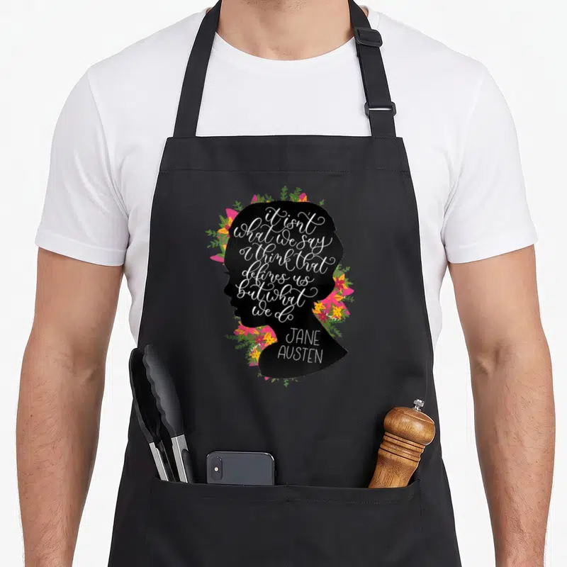 Fan jane austen apron - Black female silhouette filled with white quote text surrounded by pink yellow and green flowers — shown on a black cotton canvas apron against a white background