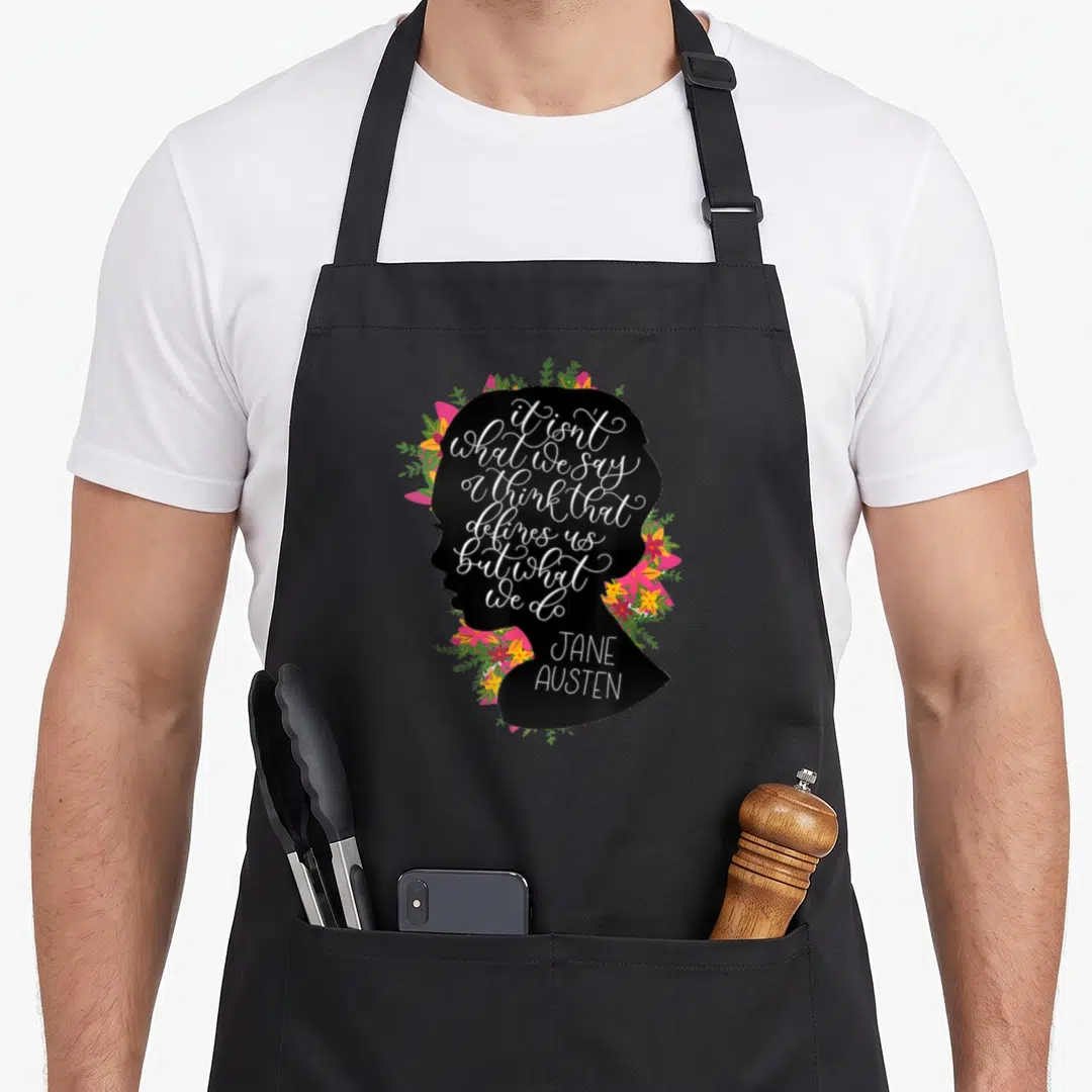 Fan jane austen apron - Black female silhouette filled with white quote text surrounded by pink yellow and green flowers — shown on a black cotton canvas apron against a white background