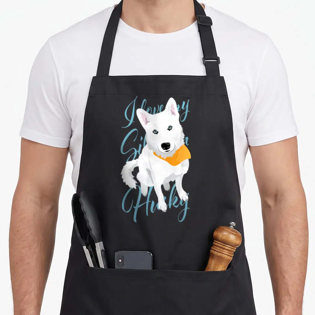 Claras husky apron - White cartoon husky with orange scarf and blue I love my Siberian Husky script — shown on a black cotton canvas apron against a white background