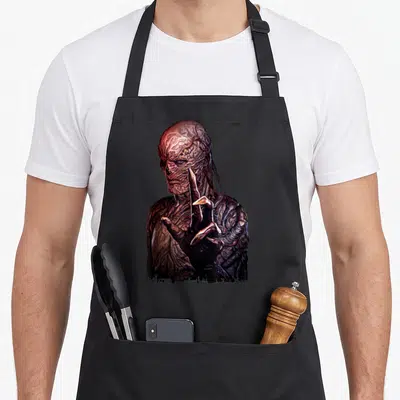Vecna hand apron - Realistic monster portrait with raised hand in brown and dark red tones — shown on a black cotton canvas apron against a white background