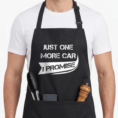Funny racing car apron - Distressed white text reading JUST ONE MORE CAR I PROMISE on grey background with curved — shown on a black cotton canvas apron against a white background