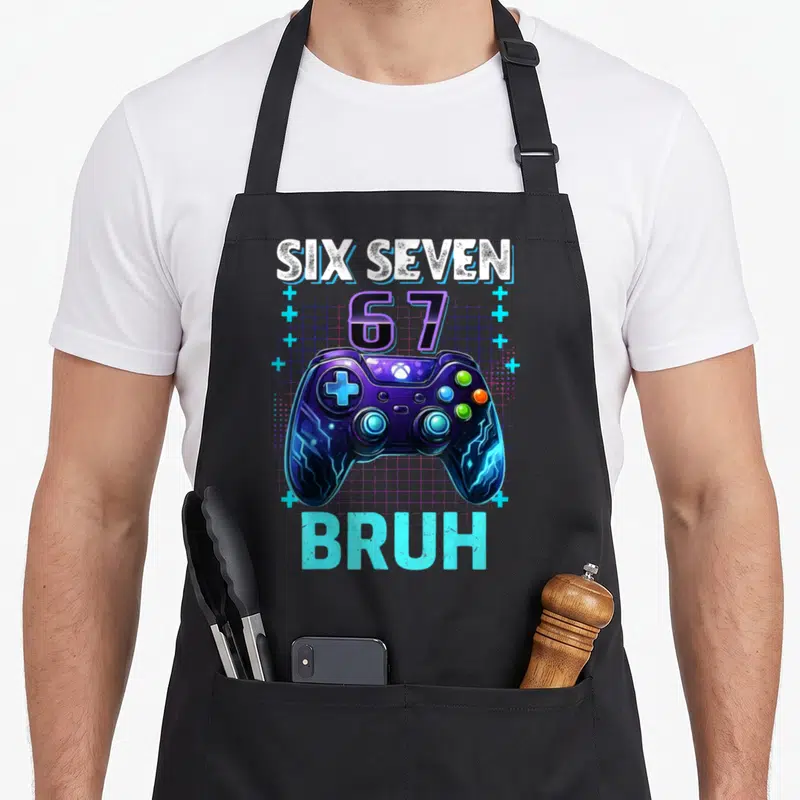 Seven bruh birthday apron - Purple game controller with SIX SEVEN 67 BRUH text and blue grid background — shown on a black cotton canvas apron against a white background