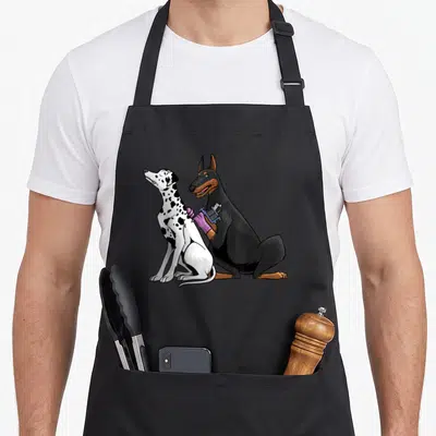 Artist dog apron - Cartoon doberman tattooing dalmatian back with purple gloves and machine — shown on a black cotton canvas apron against a white background