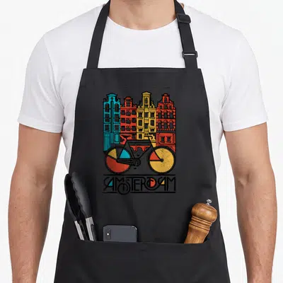 Jersey bicycle apron - Four colorful buildings behind a bicycle with AMSTERDAM text at the bottom — shown on a black cotton canvas apron against a white background