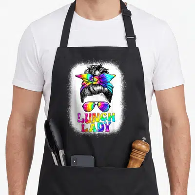Messy lunch lady apron - Cartoon woman's head with tie-dye bow and sunglasses above LUNCH LADY text on splatter — shown on a black cotton canvas apron against a white background