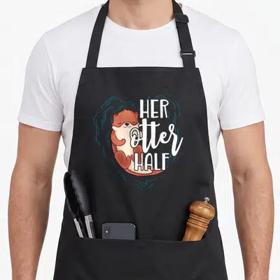 Otter valentine's day apron - Cartoon brown otter with blue swirl heart and white text HER OTTER HALF — shown on a black cotton canvas apron against a white background