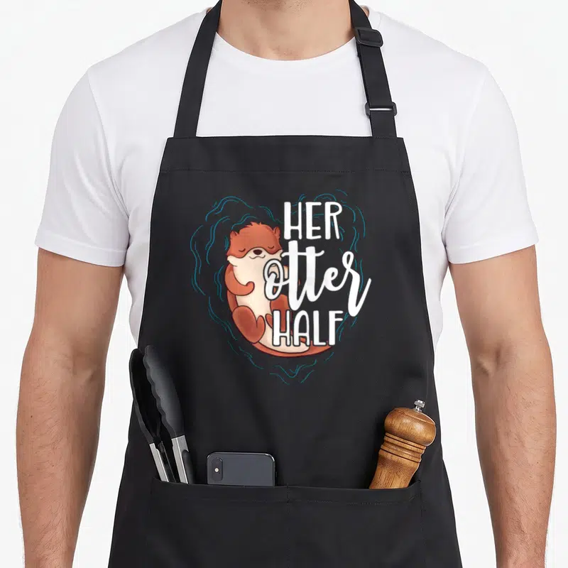Otter valentine's day apron - Cartoon brown otter with blue swirl heart and white text HER OTTER HALF — shown on a black cotton canvas apron against a white background