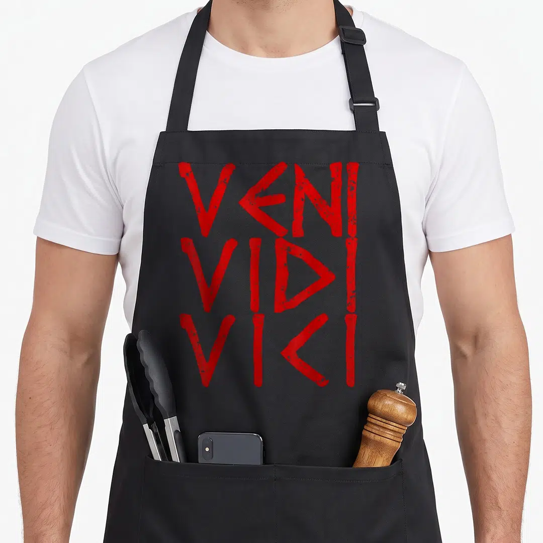 Vidi caesar apron - Red distressed VENI VIDI VICI text stacked in three lines — shown on a black cotton canvas apron against a white background