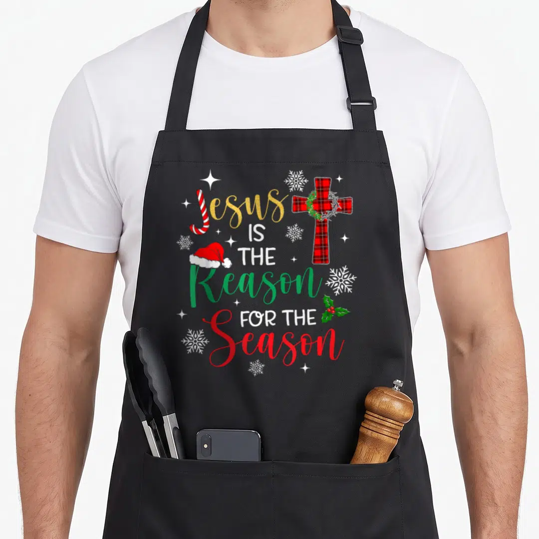 Jesus reason christmas apron - Stacked text Jesus is the reason for the season with plaid cross and candy cane — shown on a black cotton canvas apron against a white background
