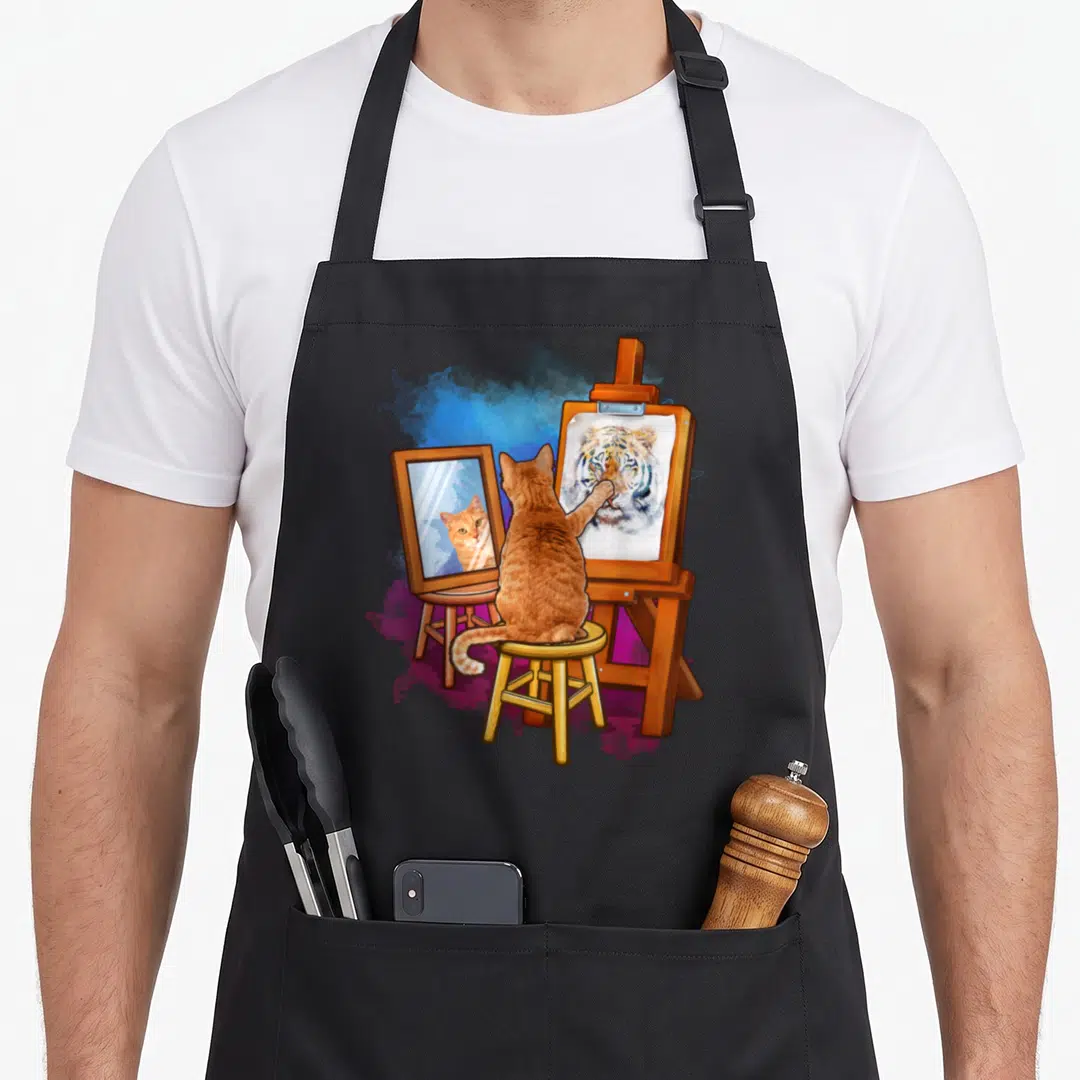 Cat artistic apron - Orange cat painting tiger portrait on easel with mirror reflection in cartoon style — shown on a black cotton canvas apron against a white background