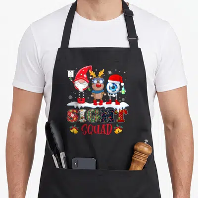 Sight christmas gnome apron - Three cartoon eye characters on snowbank above SIGHT SQUAD text with bells — shown on a black cotton canvas apron against a white background