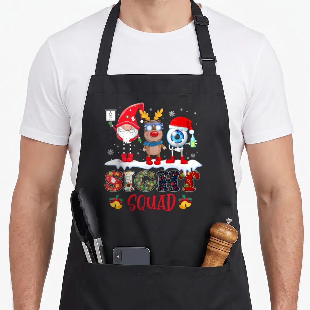 Sight christmas gnome apron - Three cartoon eye characters on snowbank above SIGHT SQUAD text with bells — shown on a black cotton canvas apron against a white background