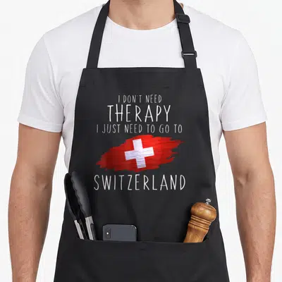 Pride swiss apron - White text reading I don't need therapy next to a red brushstroke flag with a white cross — shown on a black cotton canvas apron against a white background