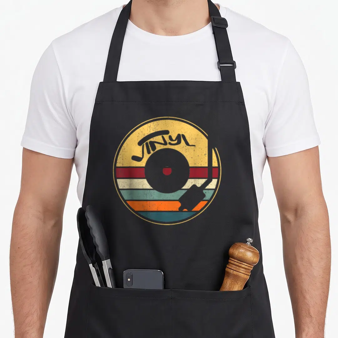 Funny record vinyl apron - Retro vinyl record graphic with arched VINYL text over yellow, red, teal, orange, and grey — shown on a black cotton canvas apron against a white background
