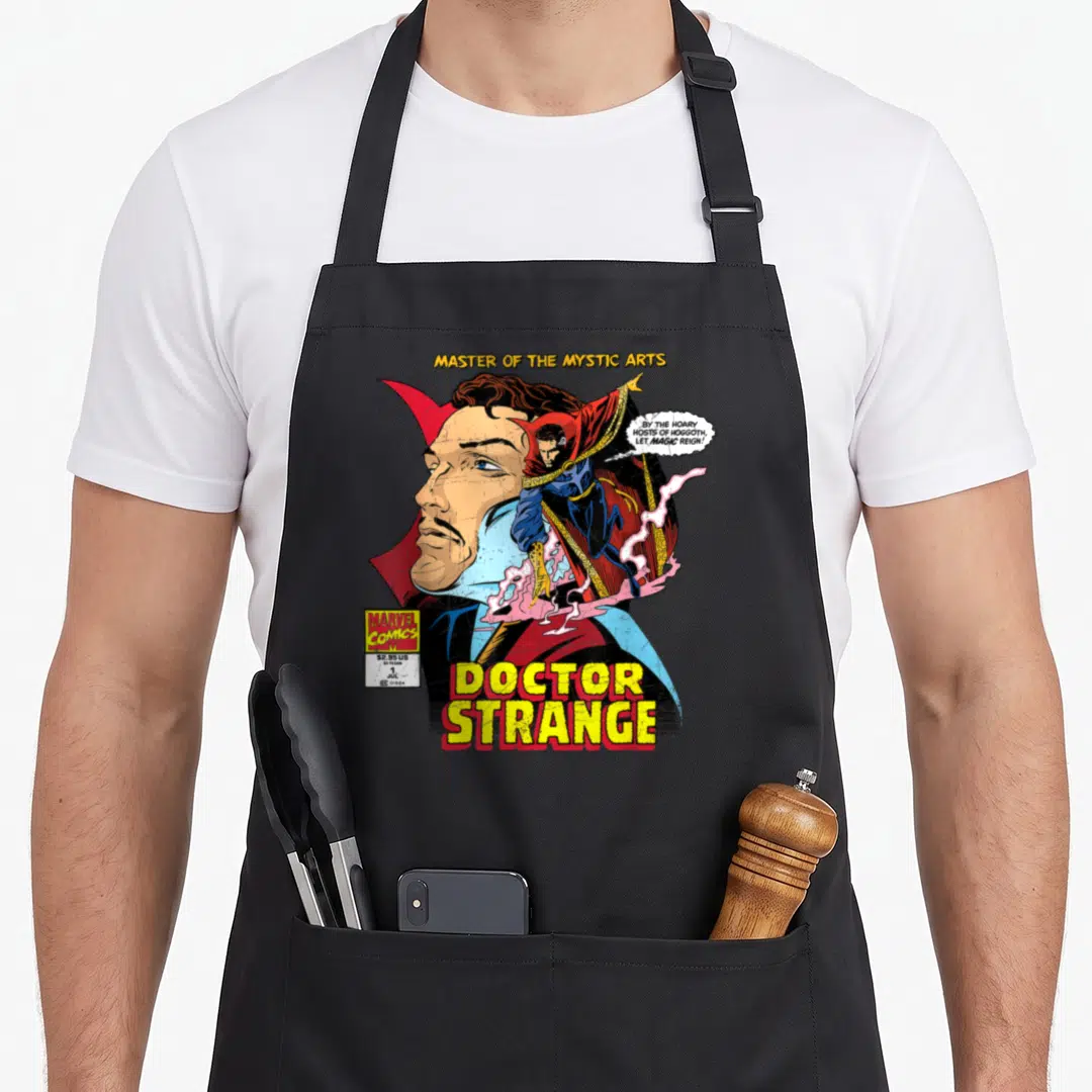 Comic doctor apron - Doctor Strange comic cover with large face, full body figure, and yellow title text — shown on a black cotton canvas apron against a white background
