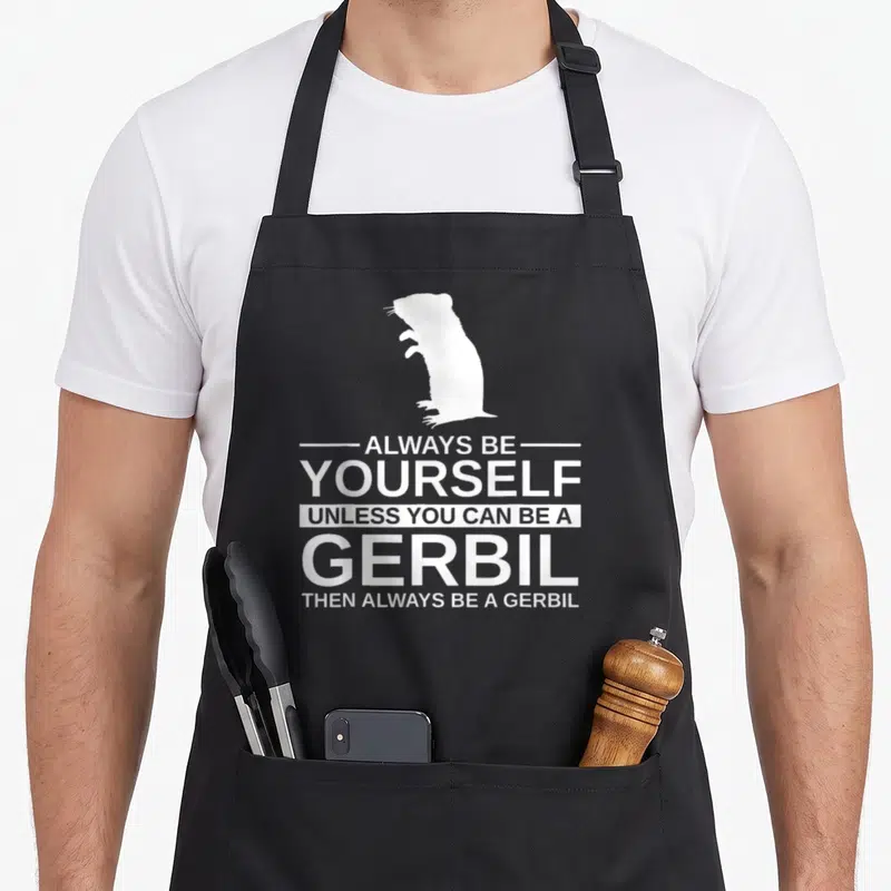 Alway pet apron - White gerbil silhouette above stacked text ALWAYS BE YOURSELF UNLESS YOU CAN BE A GERBIL — shown on a black cotton canvas apron against a white background