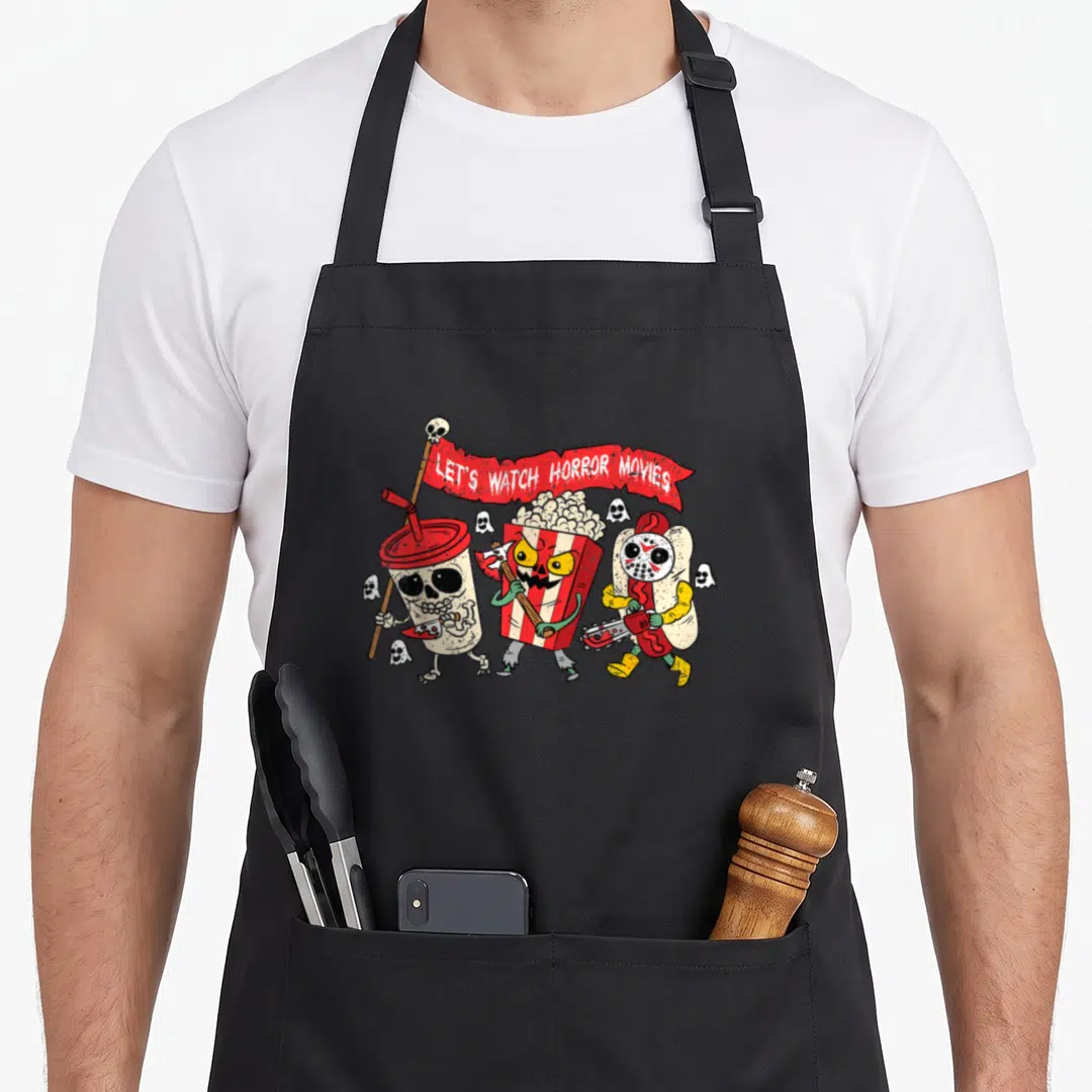 Watch skeleton apron - Three cartoon snacks holding weapons under a red banner reading LET'S WATCH HORROR MOVIES — shown on a black cotton canvas apron against a white background