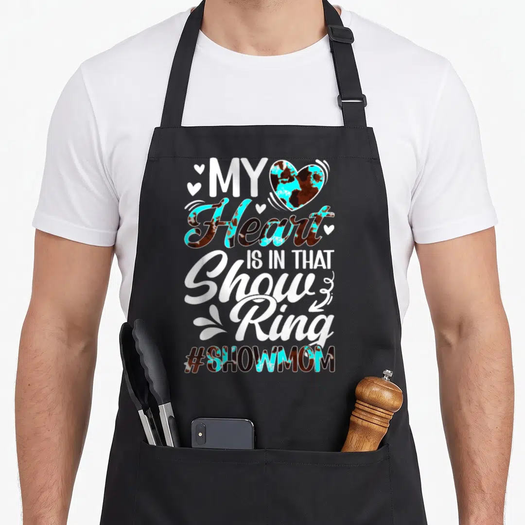Ring cooking mama apron - Stacked text My Heart IS IN THAT Show Ring with cow print heart and hashtag — shown on a black cotton canvas apron against a white background