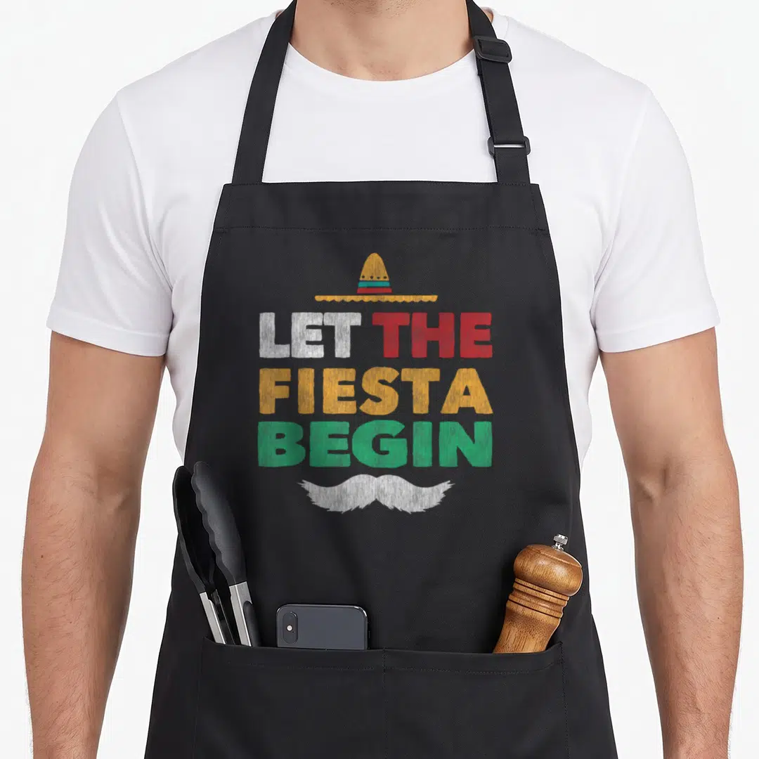 Fiesta cinco mayo mexican apron - Distressed text LET THE FIESTA BEGIN with sombrero above and mustache below in white — shown on a black cotton canvas apron against a white background