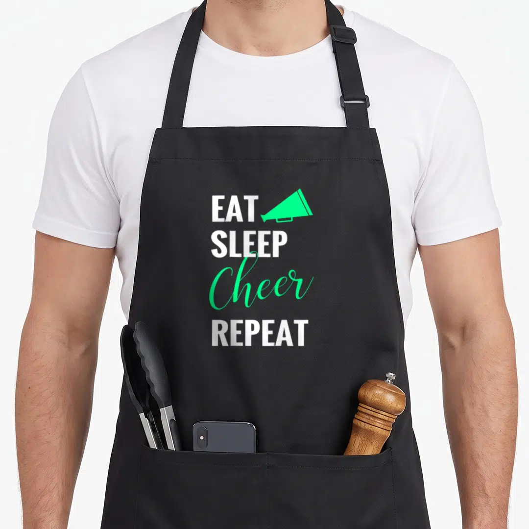 Eat cheer apron - Stacked text EAT SLEEP Cheer REPEAT with green megaphone icon — shown on a black cotton canvas apron against a white background