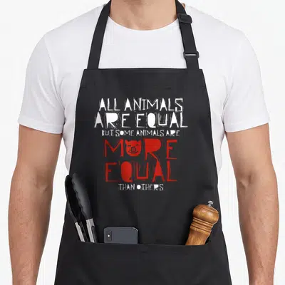 Political farm aprons - Distressed white and red text quote with red pig head inside the word More on six lines — shown on a black cotton canvas apron against a white background